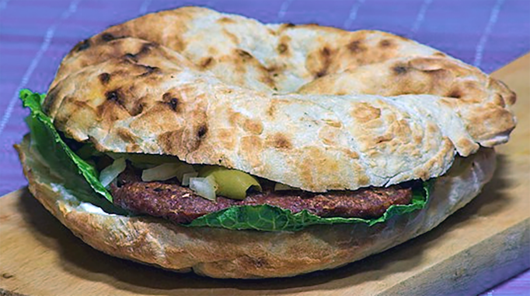 Pljeskavica meat patty served in a split lepinja flatbread shown on a plank of wood