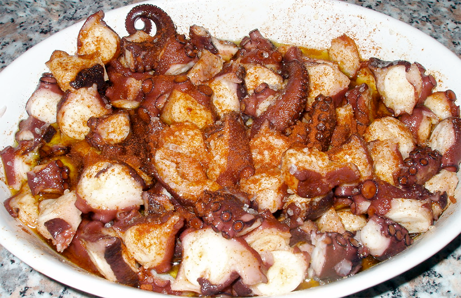 Chunks of boiled octopus served in a white dish with a garnish of olive oil and paparka