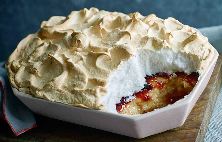 queen of puddings in a ceramic baking dish with a corner removed to show the filling