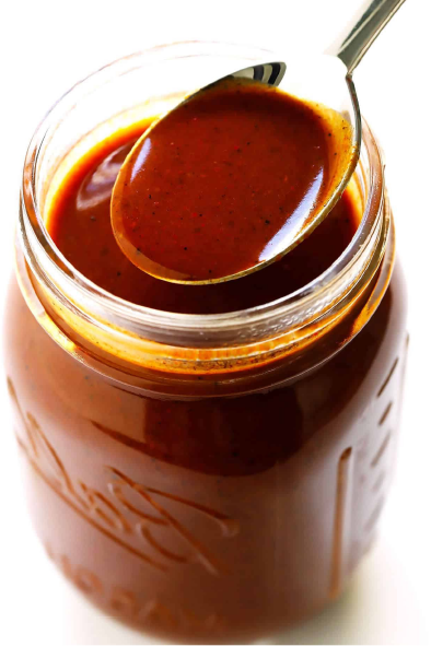 red enchilada sauce in a jar with a spoonful of the sauce on top