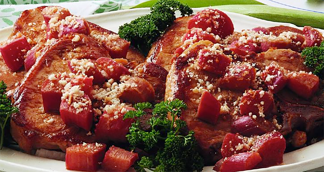 pork chops cooked with rhubarb in a casserole served topped with the rhubarb and garnished with curly parsley