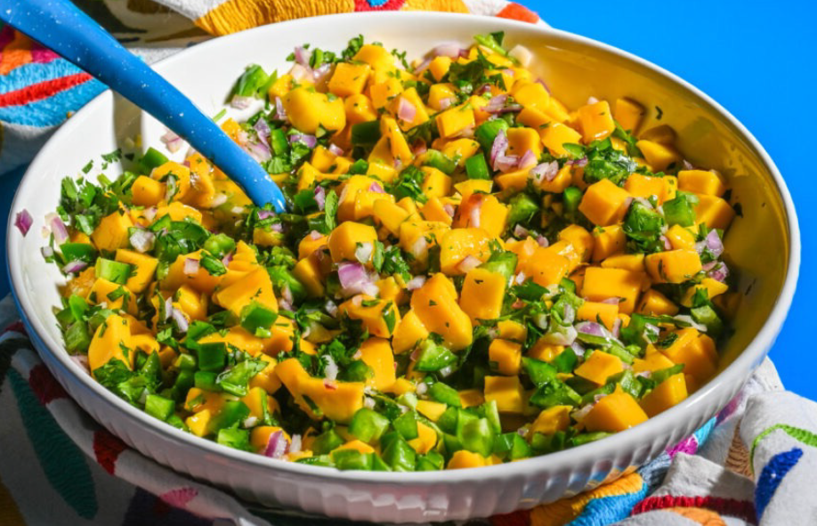 Mexican mango salsa in a white bowl with a blue spoon
