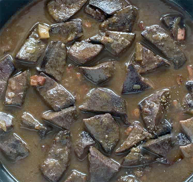 cubed liver and onions in thick gravy in a cast iron pan