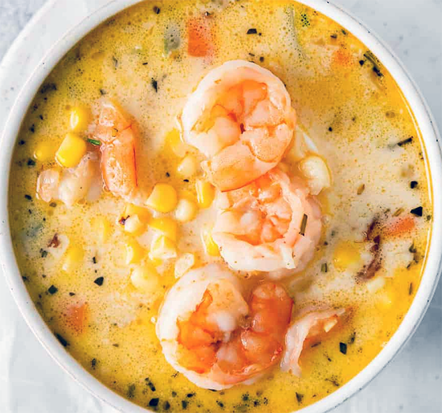 shrimp and corn chowder served in a bowl garnished with overlapping prawns
