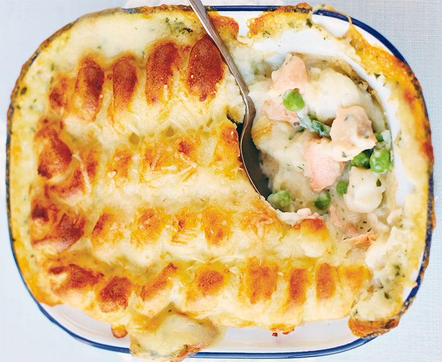 mash topped fisherman's pie in a baking dish with one corner removed to show the fish and pea filling