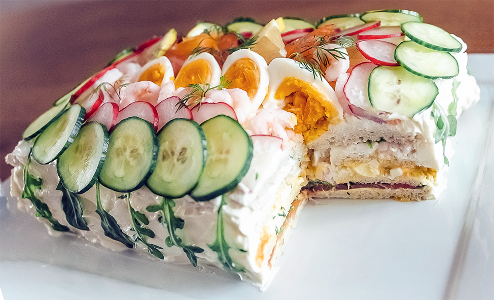 smørbrødterte arranged on a dish with a square piece removed to reveal the fillings