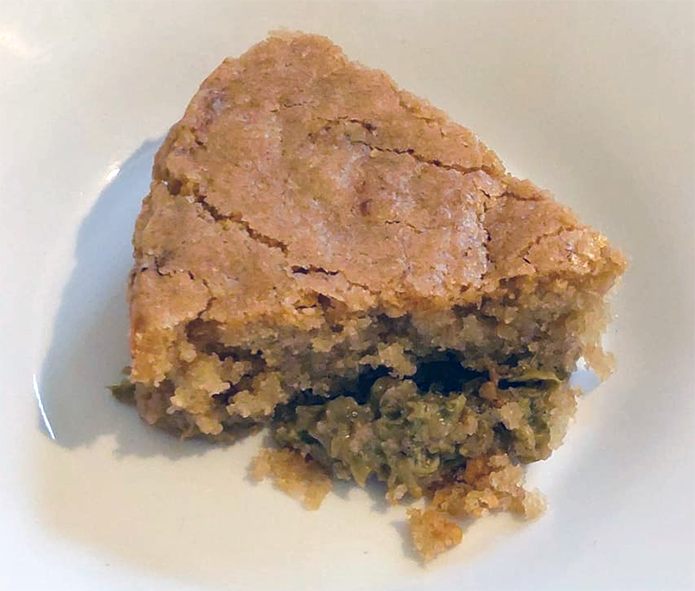 wedge of sponge-topped japanese knotweed pudding in a white dessert plate with some of the excess knotweed base before the cake