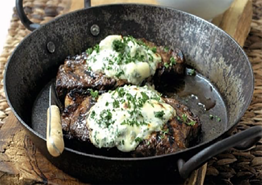 two steaks with a blue cheese and creme fraishe topping frying in a pan