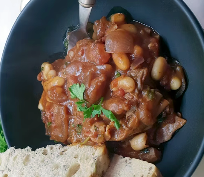 stew of trooping funnel and cannellini beans in a tomato base served in a bowl with a spoon and bread