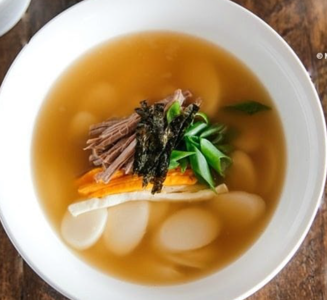 Korean rice cake soup served in a bowl garnished with carrot strips and shredded beef