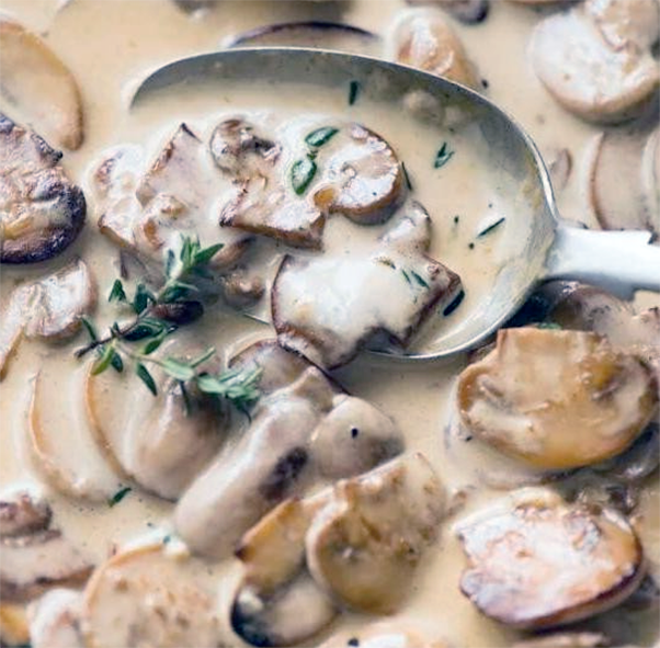 wild country mushrooms in a serving dish with a sprig of thyme lifted with a large spoon