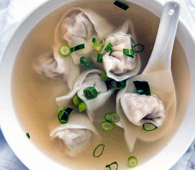 wonton dumplings in a light broth garnished with spring onions served in a white bowl with a Chinese spoon
