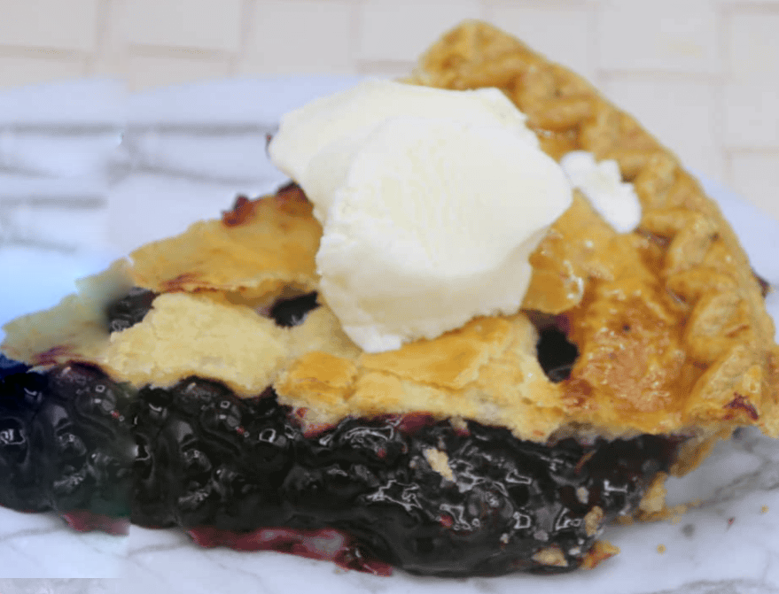 slice of air fryer bilberry pie on a marble worktop served topped with a scoop of vanilla ice cream
