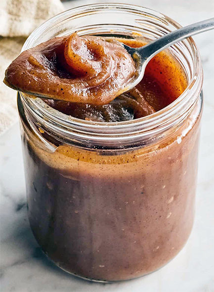 apple butter in a jam jar with some on a spoon on top of the jar