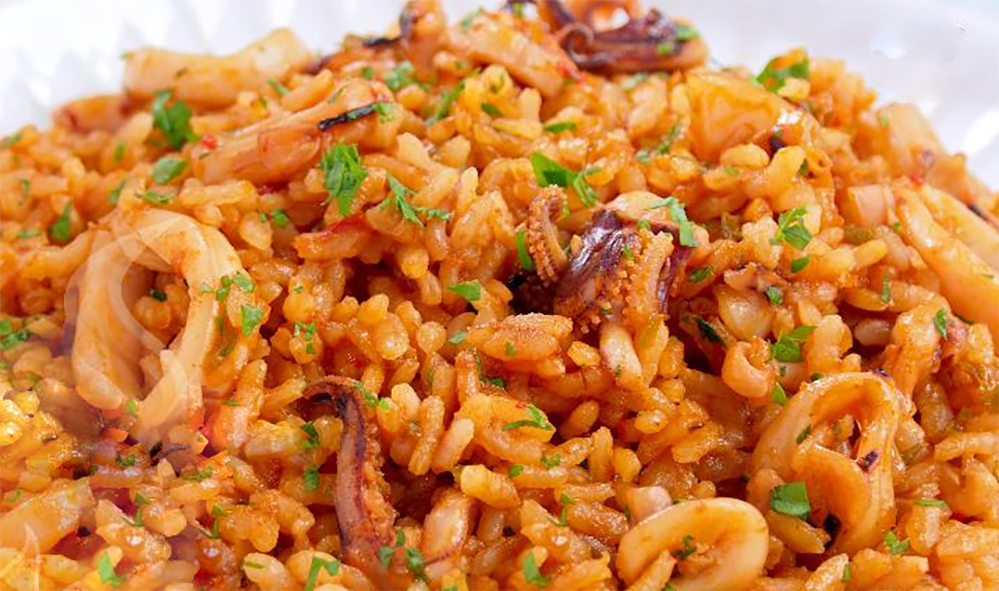 short grain rice with squid and mixed seafood garnished with chopped parsley served in a white dish