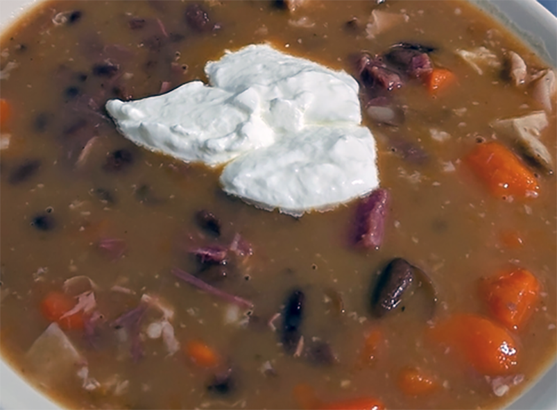 bean soup with knuckle of pork served garnished with sour cream in a bowl