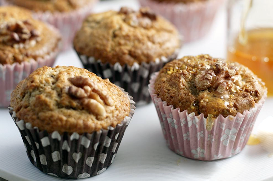 banana muffins topped with walnuts served on a dish drizzled with honey
