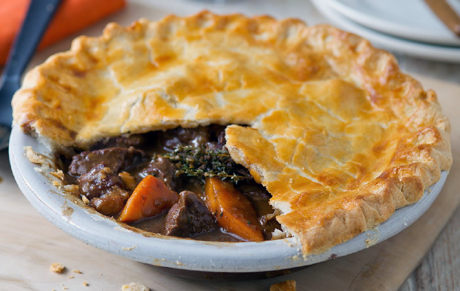 beef and guiness pie with carrot in a baking dish with a pastry crust with a wedge of pastry removed to reveal the filling