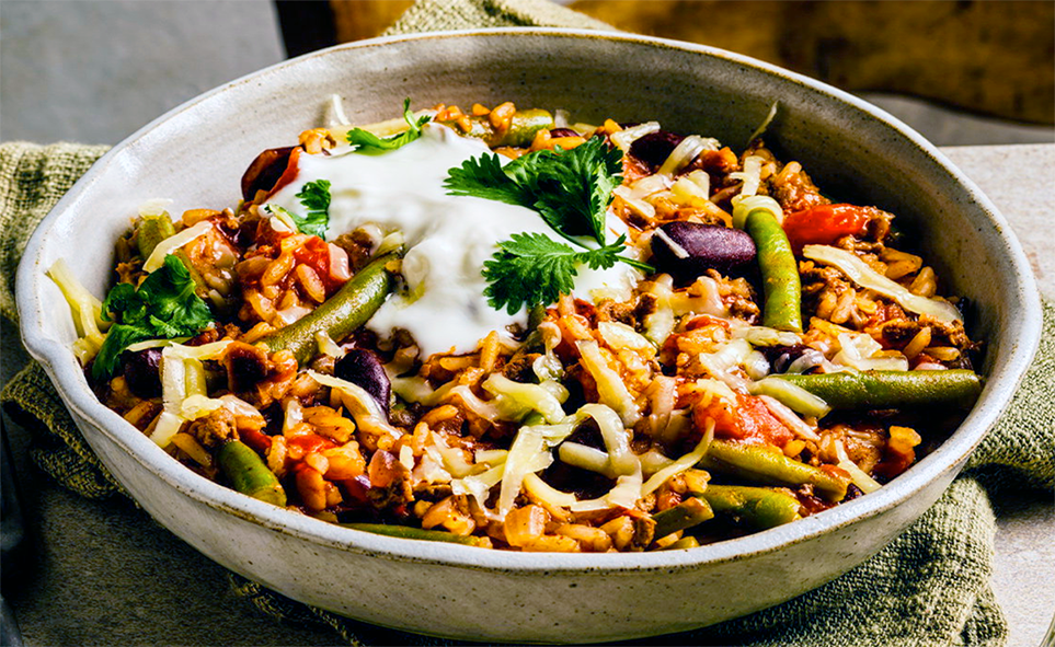 bowl of rice with minced venison, beans and vegetables served garnished with sour cream and coriander leaves