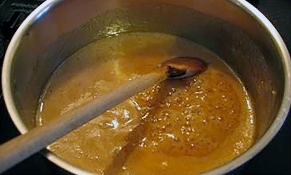 Brown chaudfroid sauce simmering in a steel pan with a wooden spoon