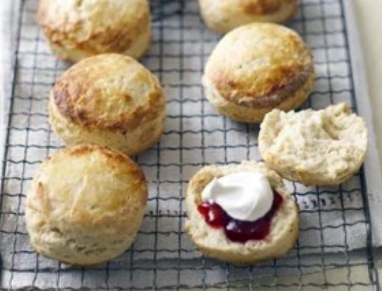 buttermilk scones on a wire cooling rack with one split open and spread with jam and clotted cream
