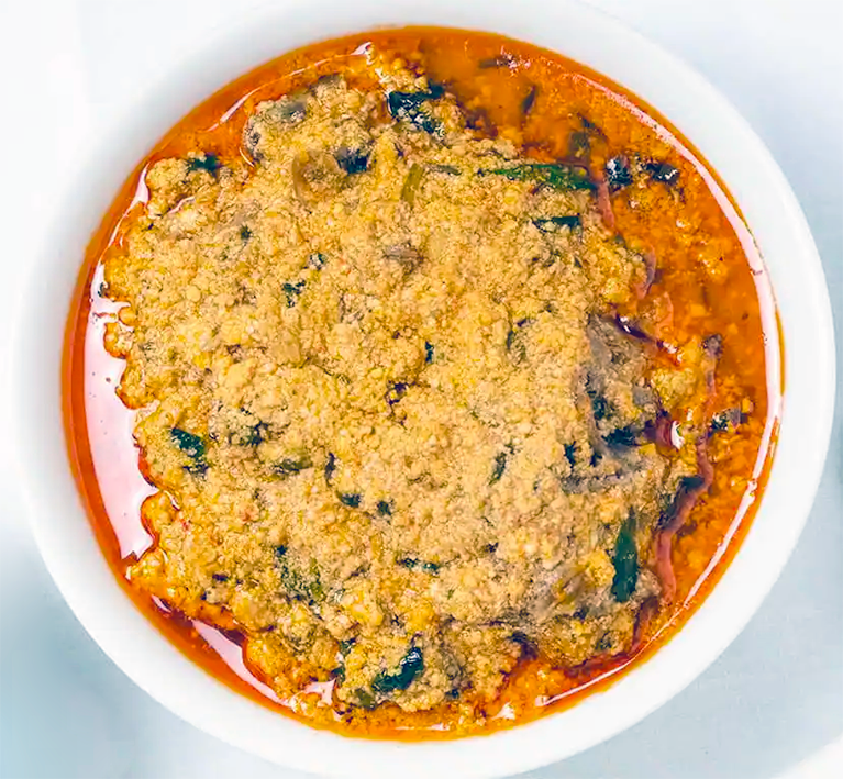cabbage egusi soup with meat in an oil-based sauce coloured with paprika served in a shallow white bowl