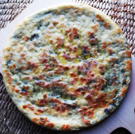 flatbread filled with cheese and beetroot leaves on a chopping board