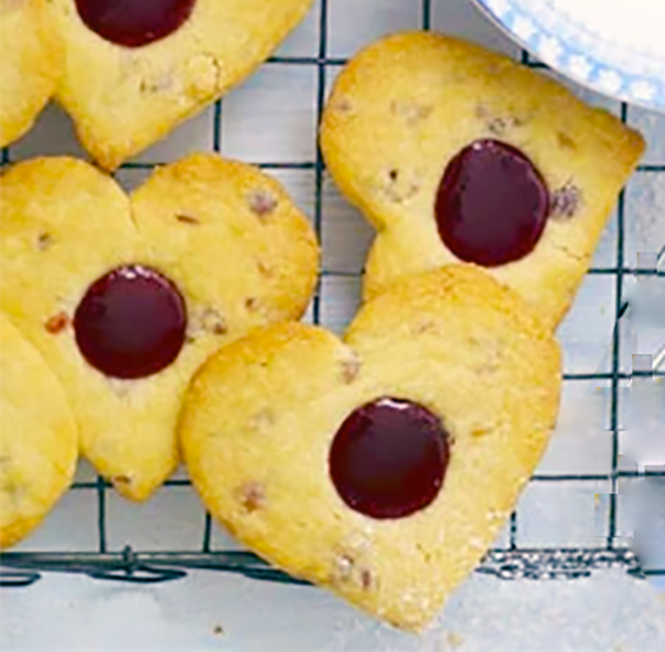 cherry shortbread biscuits in the shape of a heart with a thumbprint of cherry jam in the centre cooling on a wire rack