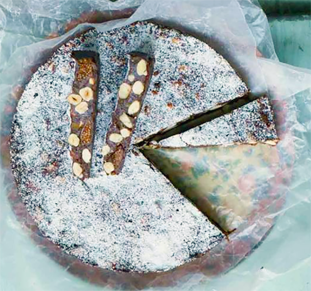 Chocolate panforte cake on a plate lined with greaseproof paper with two slices of cake on top
