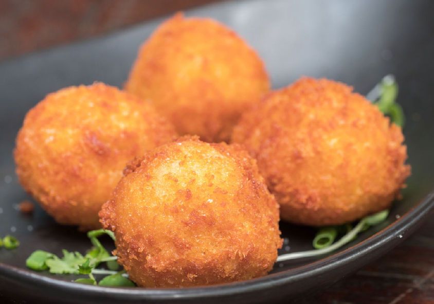 breaded colcannon croquette balls in a dish with micro greens