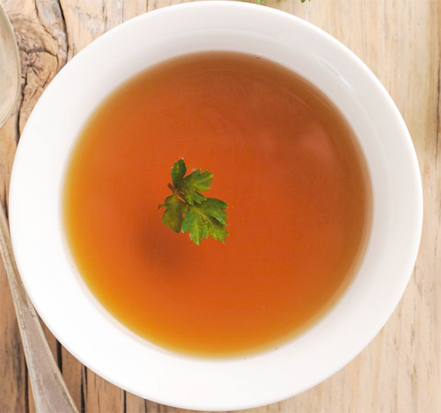 Clear chicken consomme in a white bowl with a sprig of flat-leaf parsley