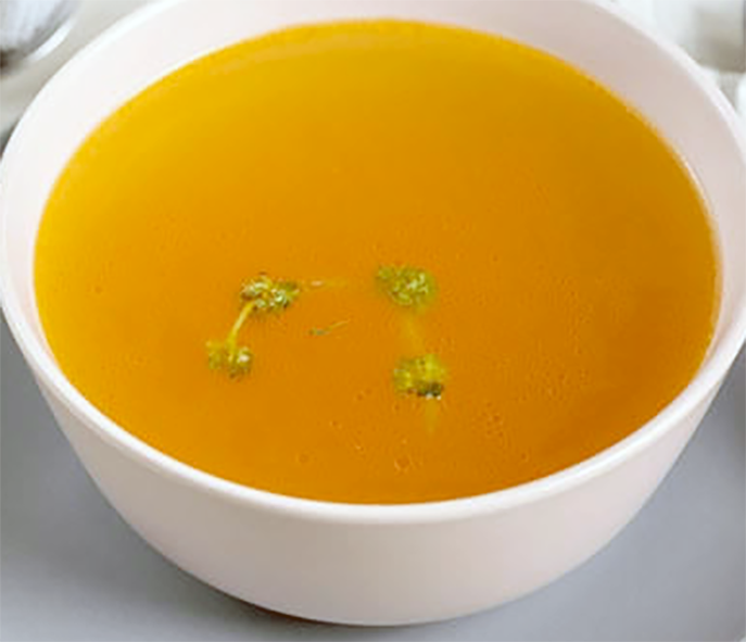 Clear beef consomme in a white bowl with a two sprigs of curly parsley