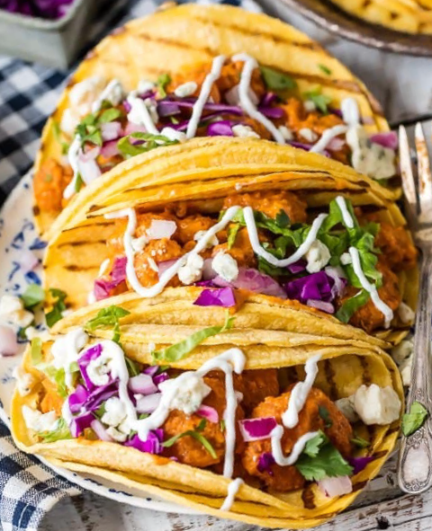 popcorn shrimp in buffalo sauce served in taco shells with red cabbage, lettuce, blue cheese, sour cream and a drizzle of ranch dressing
