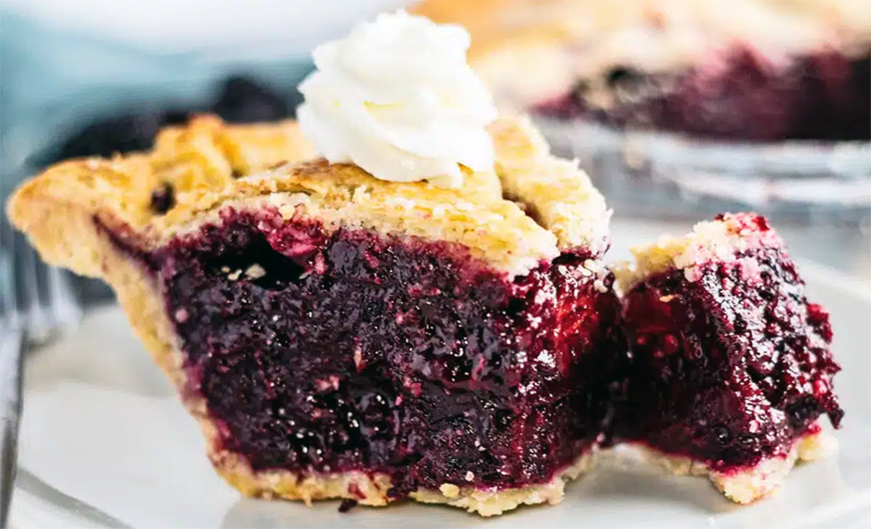 wedge of deep-filled crowberry pie on a plate with cream