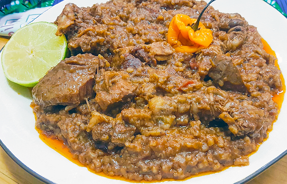 steamed rice and ground panut sauce with smoked and dried fish served on a plate with a lime slice and hot chilli garnish