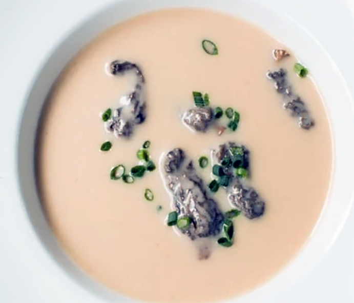 cream-coloured morel bisque garnished with morels and chives in a white soup bowl