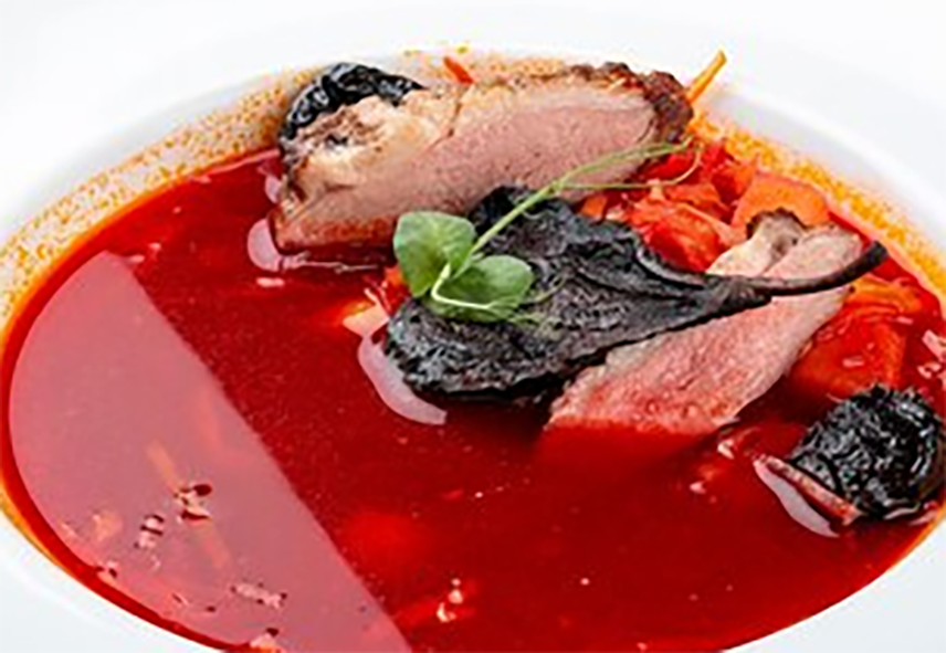 Borscht served in a bowl with slices of duck meat