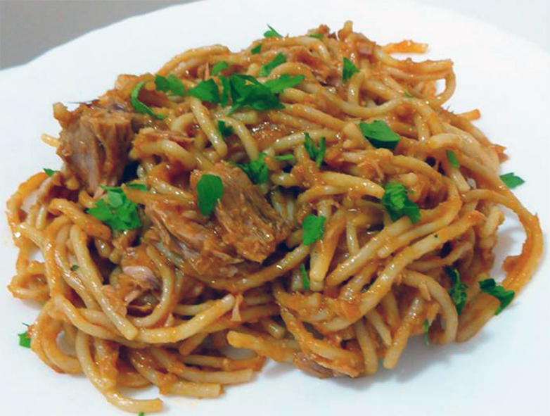 spaghetti in a tomato sauce with tinned tuna served on a plate and garnished with flat-leaf parsely