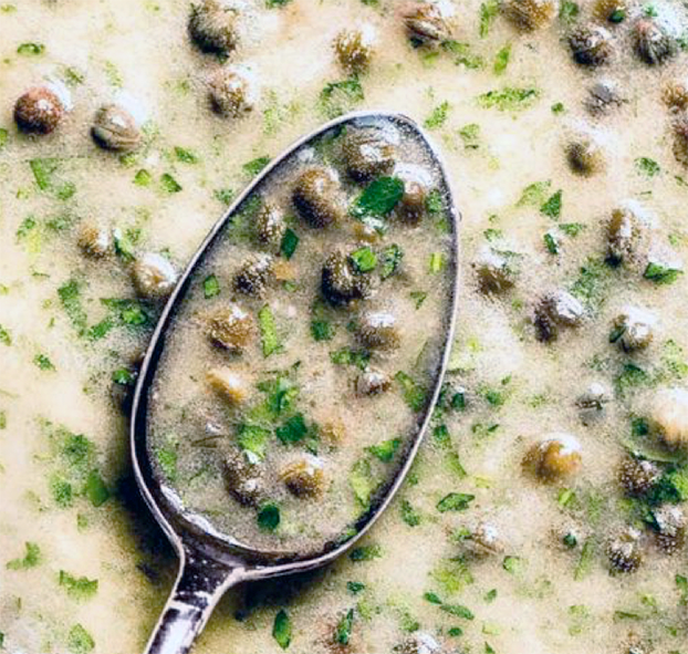 Spoon lifting some of the capers in a background of the white caper sauce