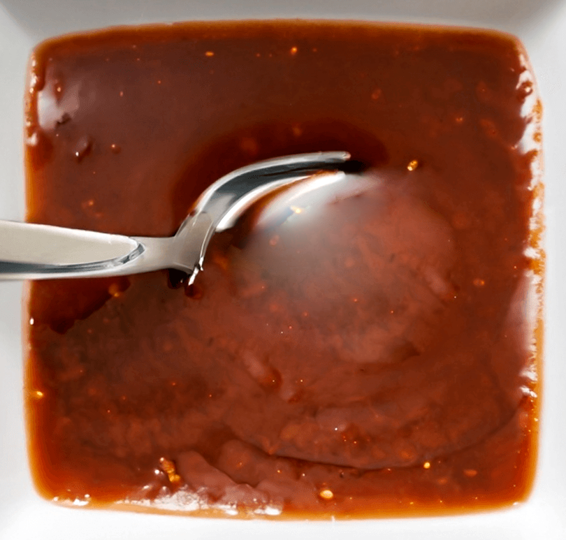 Devil's sauce in a square white sauce dish with a spoon