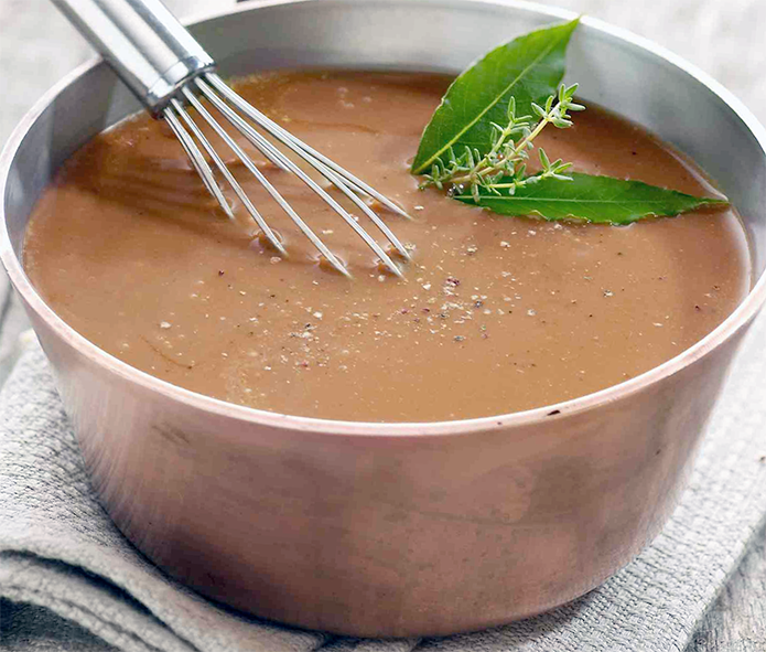 Italian Sauce in a saucepan with a whisk, bay leafs and a sprig of thyme