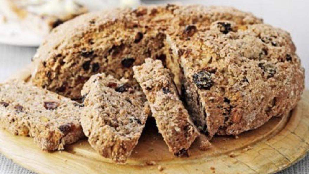 fruit and spice soda bread loaf on a chopping board with three slices arranged before the loaf