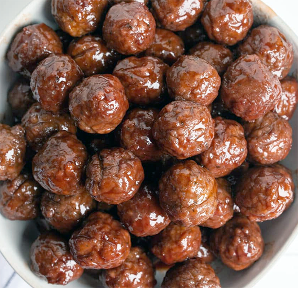 glossy grape jelly meatballs piled in a white bowl