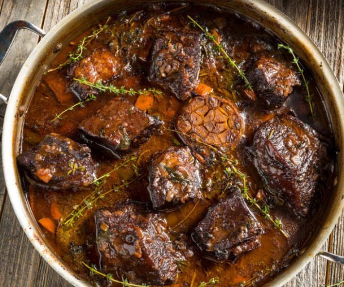beef short ribs braised in guinness with a halved garlic bulb in a casserole dish served garnished with thyme sprigs