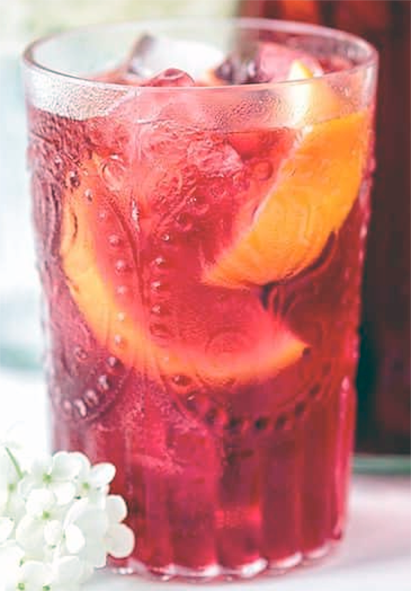 hibiscus and redcurrant tea served in a glass with orange wedges and ice