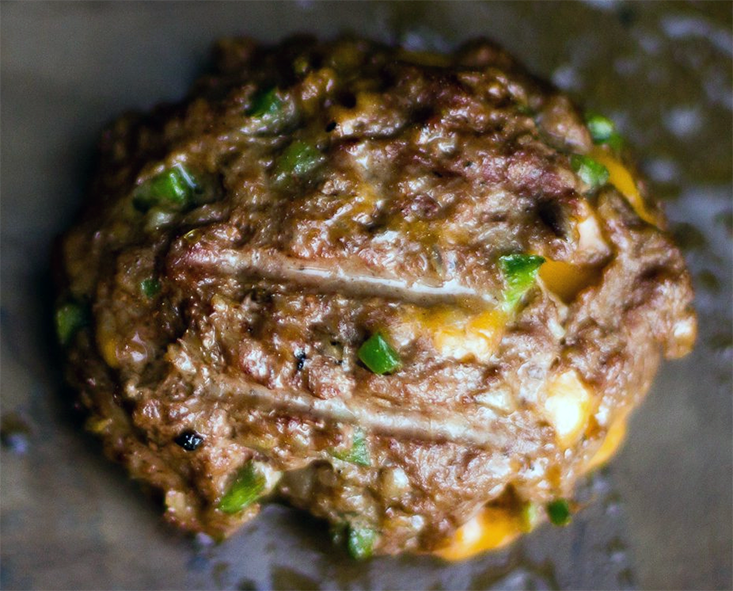 buffalo meat burger with jalapenos cooking on a griddle