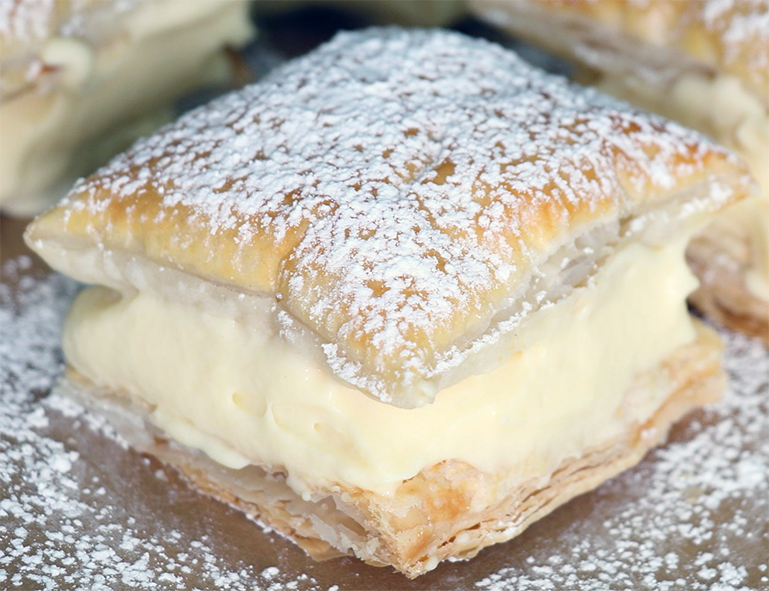 square of Polish custard pillows served on a plate dusted with icing sugar