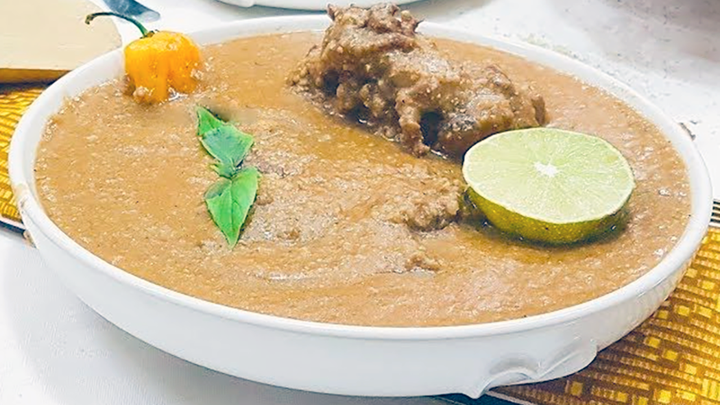 yellow hibiscus stew with millet and black beans served topped with a habanero chilli, smoked and dried fish, African blue basil sprig and a slice of lime