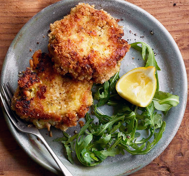 two fishcakes of leftover mash and tinned fish on a plate with rocket leaves and a lemon wedge