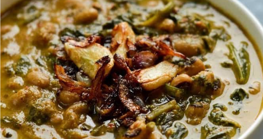 spinach and black eyed bean curry served in a white bowl with a fried pearl onion tempering